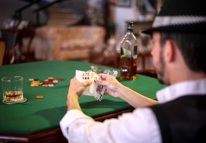 Mand spiller poker på bar med whiskey ved siden